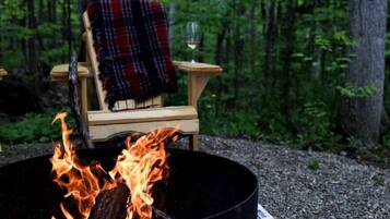 A campfire with a chair and a glass of wine in a forest setting.
