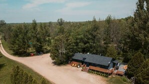 A large, single-story building with a dark roof, surrounded by a gravel driveway and dense trees.