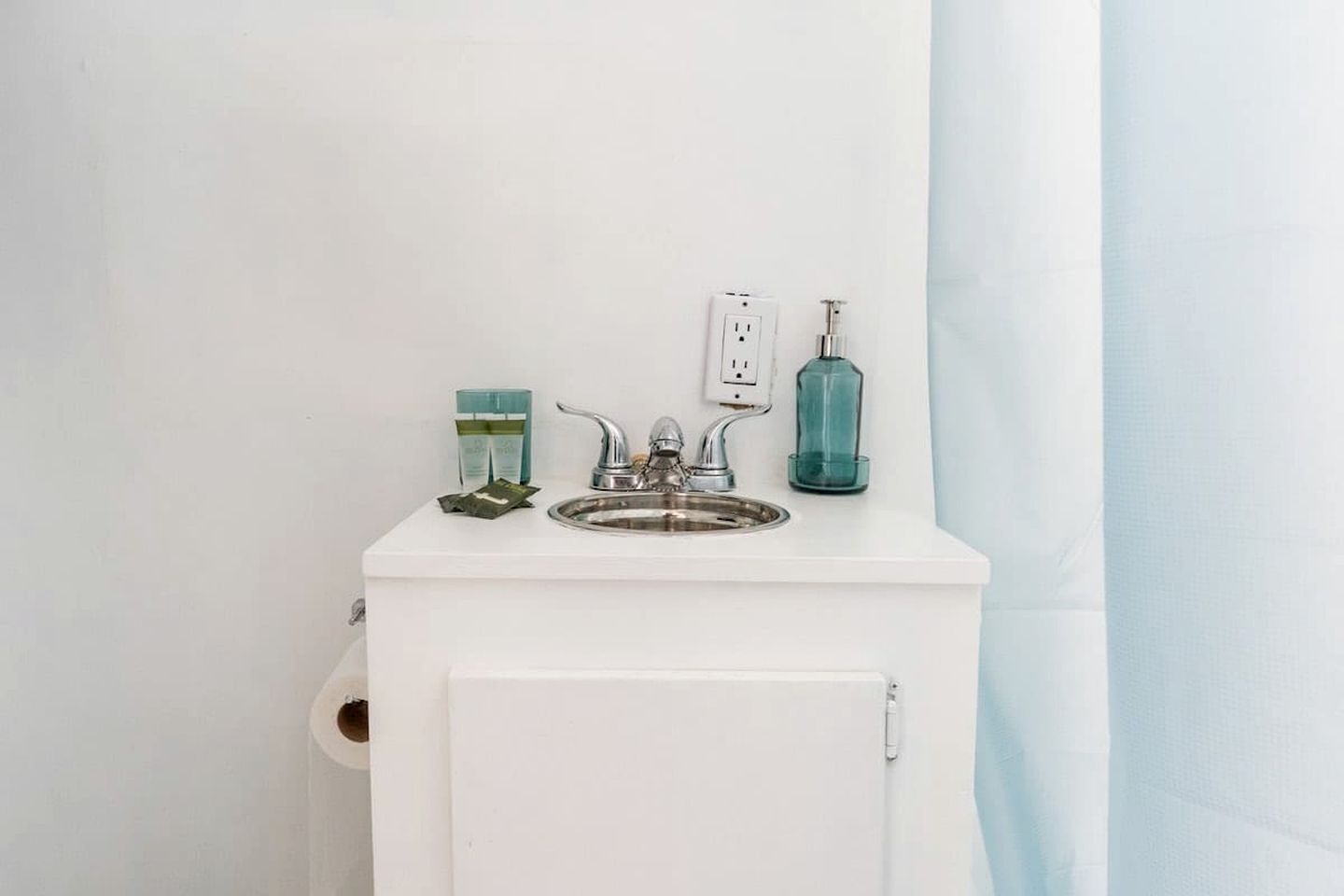 Une salle de bain avec un lavabo blanc, un robinet, un distributeur de savon et un récipient en verre.