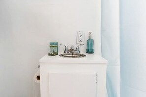 Un bagno con un lavandino bianco, un rubinetto, un dispenser di sapone e un contenitore di vetro.
