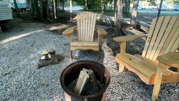 Un terrain de camping avec deux chaises Adirondack, un foyer et des arbres en arrière-plan.