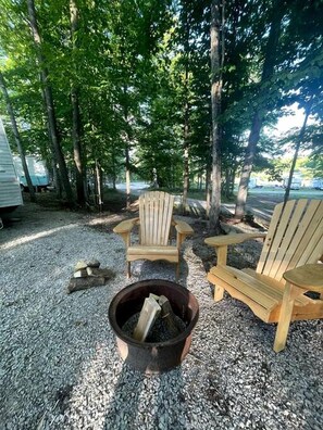 Un terrain de camping avec deux chaises Adirondack, un foyer et des arbres en arrière-plan.