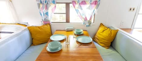 A compact living space with a wooden table set for dining, two cushioned seating areas, and a window with patterned curtains.