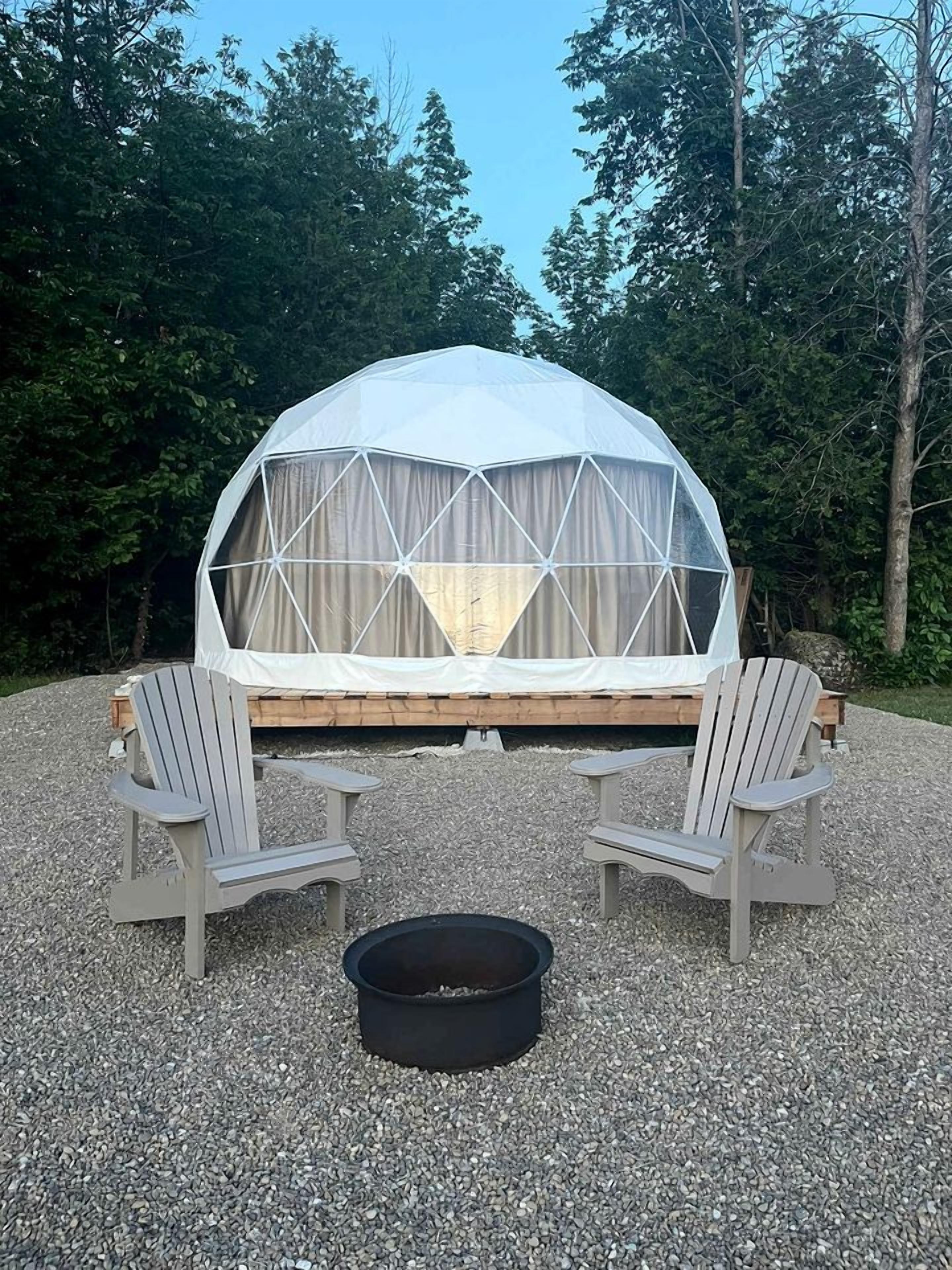 A geodesic dome tent with a wooden platform and two Adirondack chairs.
