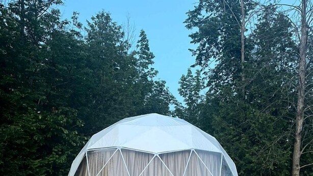 A geodesic dome tent with a wooden platform and two Adirondack chairs.