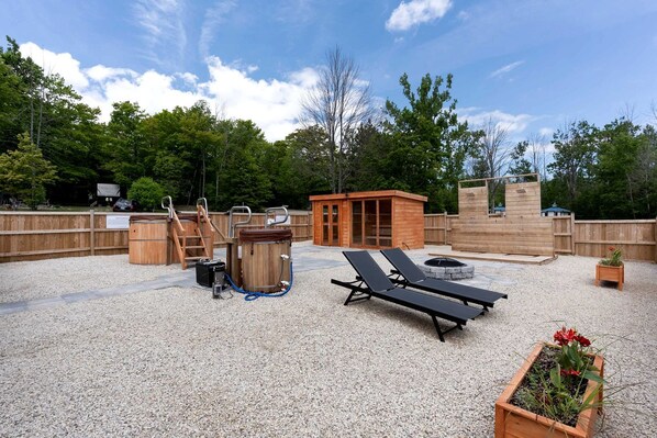 Un área de patio exterior con un jacuzzi, sillones de descanso, una terraza de madera y una pequeña estructura de madera.