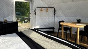 Una habitación tipo tienda de campaña con una cama, una mesa con sillas, un sillón colgante y un ventilador.