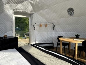 A tent-style room with a bed, a table with chairs, a hanging chair, and a fan. - Nordic Luxe Geodome Retreat with Skylight & Forest Views near Tobermory, Ontario (Miller Lake)