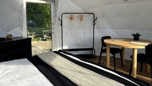 A tent-style room with a bed, a table with chairs, a hanging chair, and a fan.