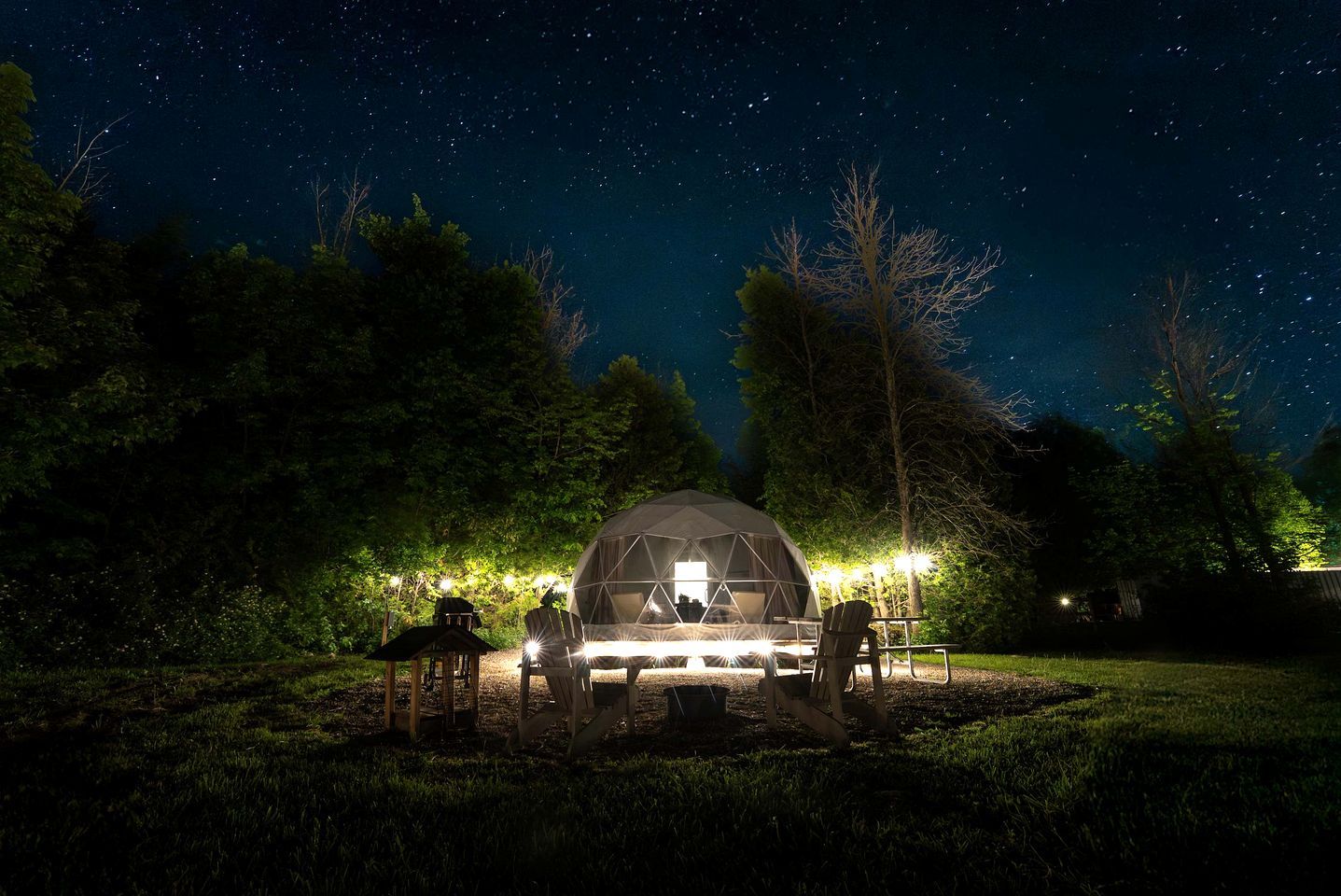A dome-shaped tent with a table and chairs in a grassy area at night.