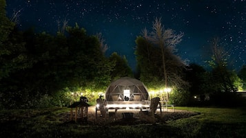 A dome-shaped tent with a table and chairs in a grassy area at night.