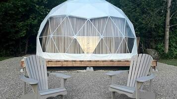 A geodesic dome tent with a wooden platform and two Adirondack chairs.