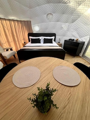 A bedroom with a bed, bedside tables, a small desk, a round wooden table with placemats, and a potted plant. - Nordic Luxe Geodome Retreat with Skylight & Forest Views near Tobermory, Ontario (Miller Lake)