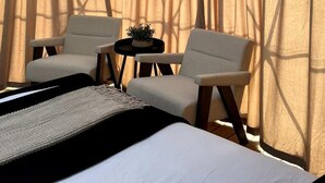 A room with a bed, two chairs, a small table with a plant, and sheer curtains.