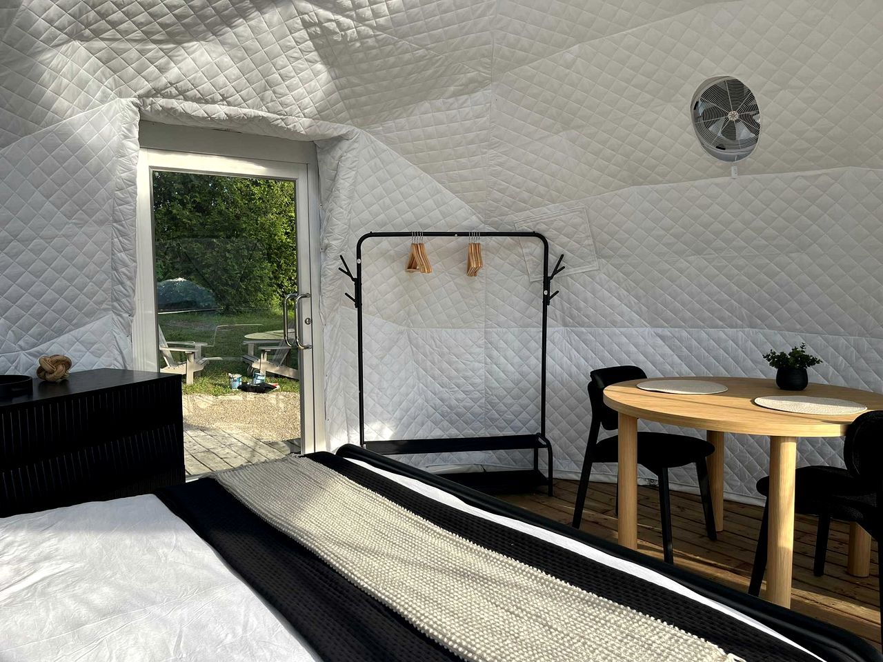 Ein Zeltraum mit Bett, Tisch mit Stühlen, einer Hängematte und einem Ventilator.