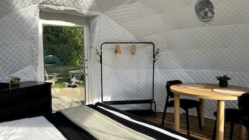 Ein Zeltraum mit Bett, Tisch mit Stühlen, einer Hängematte und einem Ventilator.