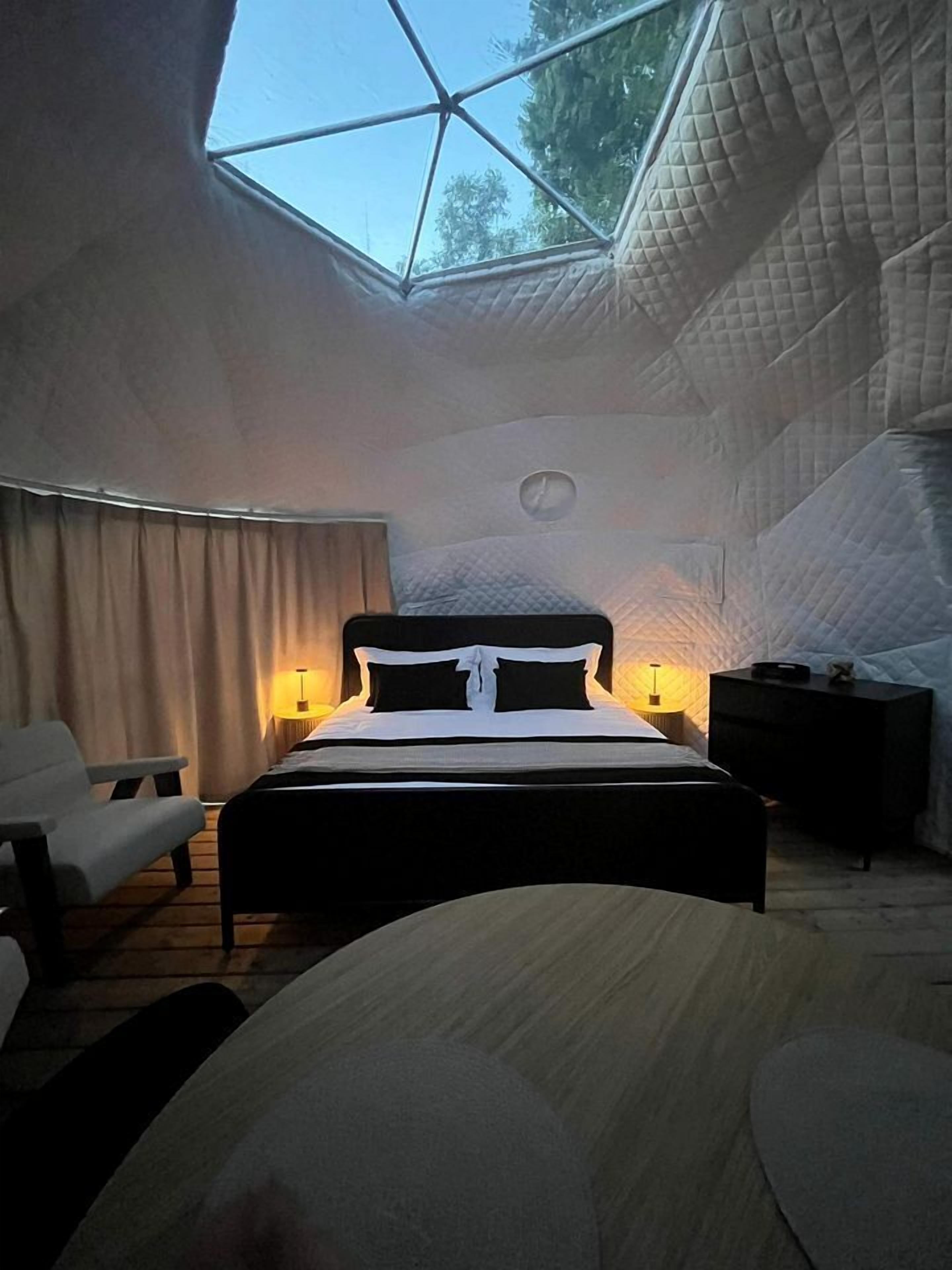 A bedroom with a skylight, a bed, a chair, and a bedside table.