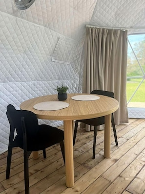 A round wooden table with two chairs, a potted plant, and a quilted wall in a tent-like structure.
