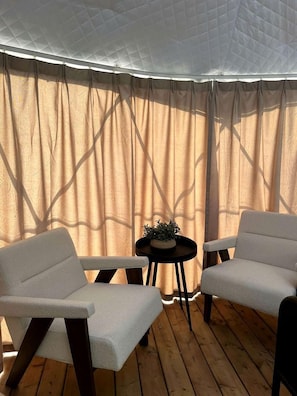 A room with a wooden floor, two white armchairs, a small round table with a plant, and sheer curtains. - Nordic Luxe Geodome Retreat with Skylight & Forest Views near Tobermory, Ontario (Miller Lake)