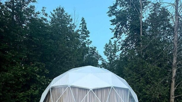 Una tienda en forma de cúpula geodésica con una plataforma de madera y dos sillas Adirondack.