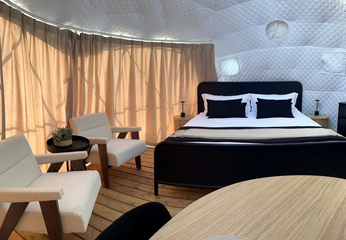 A tent-style room with a bed, two chairs, a small table, and a round table.