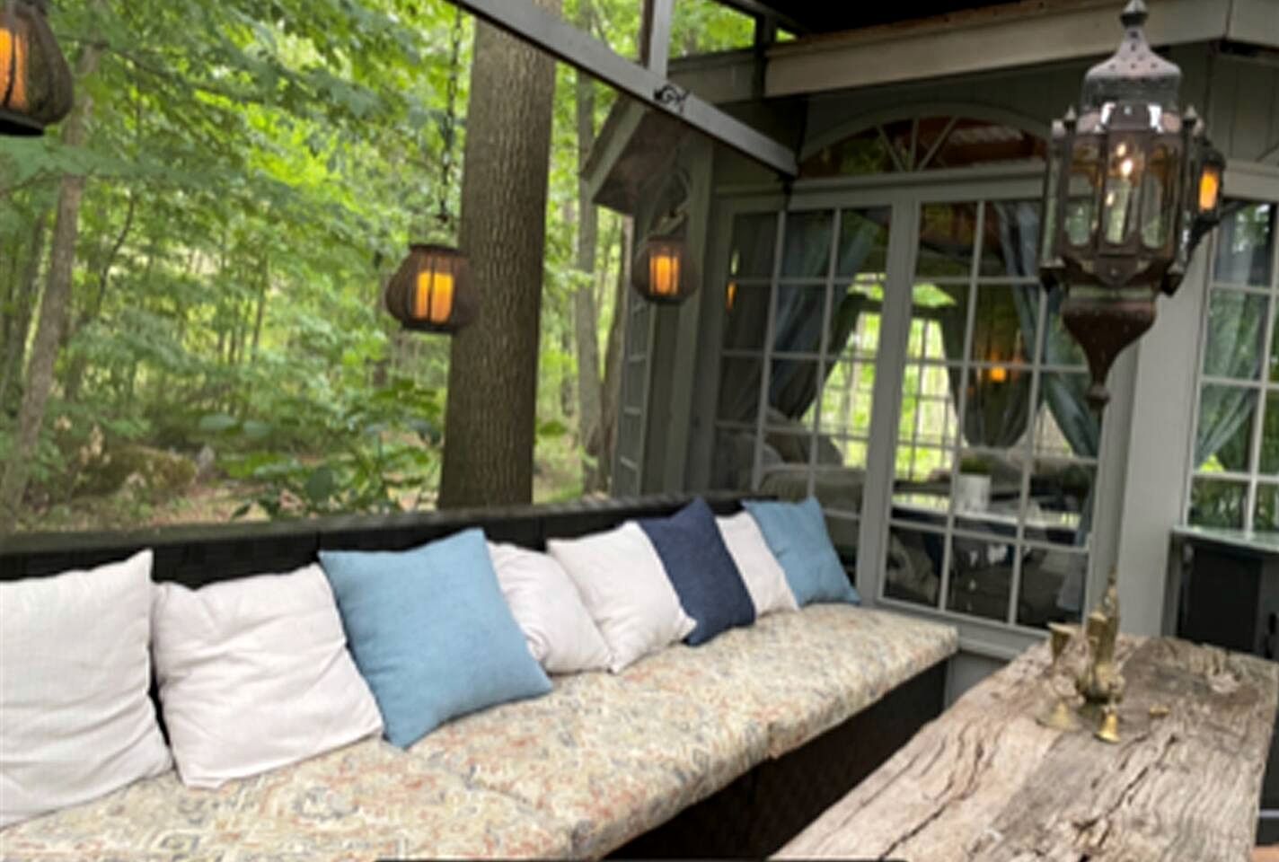 A wooden bench with cushions, a rustic table, and a glass enclosure with a forest view.