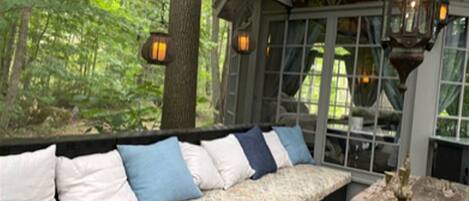 A wooden bench with cushions, a rustic table, and a glass enclosure with a forest view.