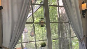A room with a table and two stools, a window with curtains, and a hanging light fixture.