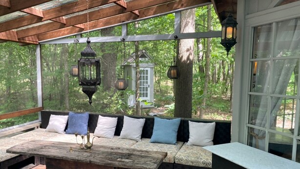 A covered outdoor seating area with a wooden table, cushioned benches, and hanging lanterns.