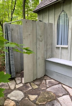 A corner of a building with a stone floor, a window with a curtain, and a wooden fence.