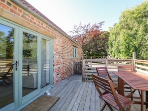 Eine Holzterrasse mit Tisch und Stühlen, ein Backsteinhaus mit Glasüren und ein Holzzaun.