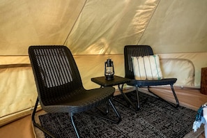 A tent with two black wicker chairs, a small table with a lantern, and a pillow with a tree design.