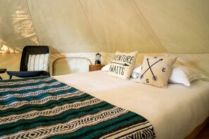 Una cama con ropa de cama estampada, dos almohadas con texto, una silla y una mesita de noche con lámpara.