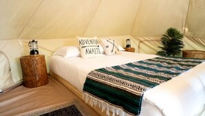 Ein Zeltunterstand mit einem Bett, Kissen, einer Decke, einer Laterne und einer kleinen Pflanze.