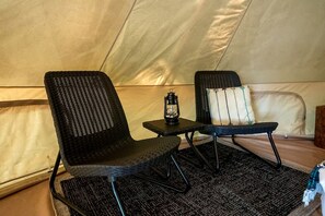 A tent with two black wicker chairs, a small table with a lantern, and a pillow with a tree design.