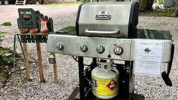 A portable grill with a propane tank, a barbecue sign, and a nearby RV.