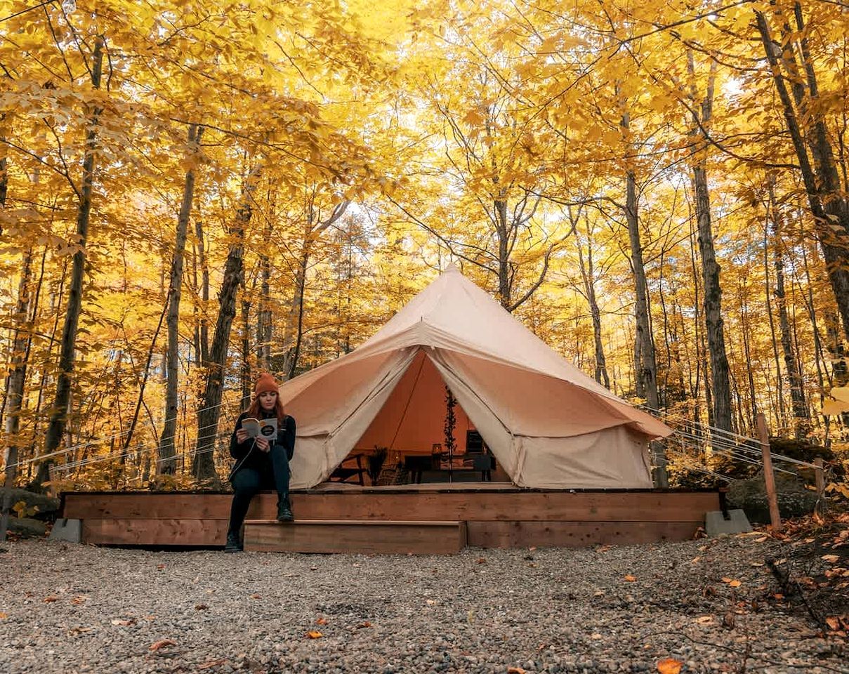 Une tente dans une forêt, avec une personne assise devant.