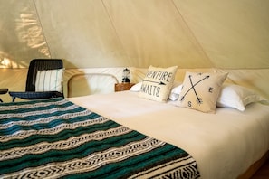 A bed with patterned bedding, two pillows with text, a chair, and a nightstand with a lamp.