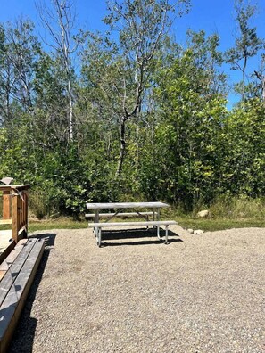 A picnic table in a natural setting with a gravel ground and trees in the background.