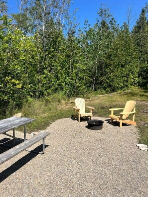A gravel area with two Adirondack chairs, a picnic table, and a fire pit. - Intimate Luxurious Bell Tent with Fire Pit in Ontario (Northern Bruce Peninsula)