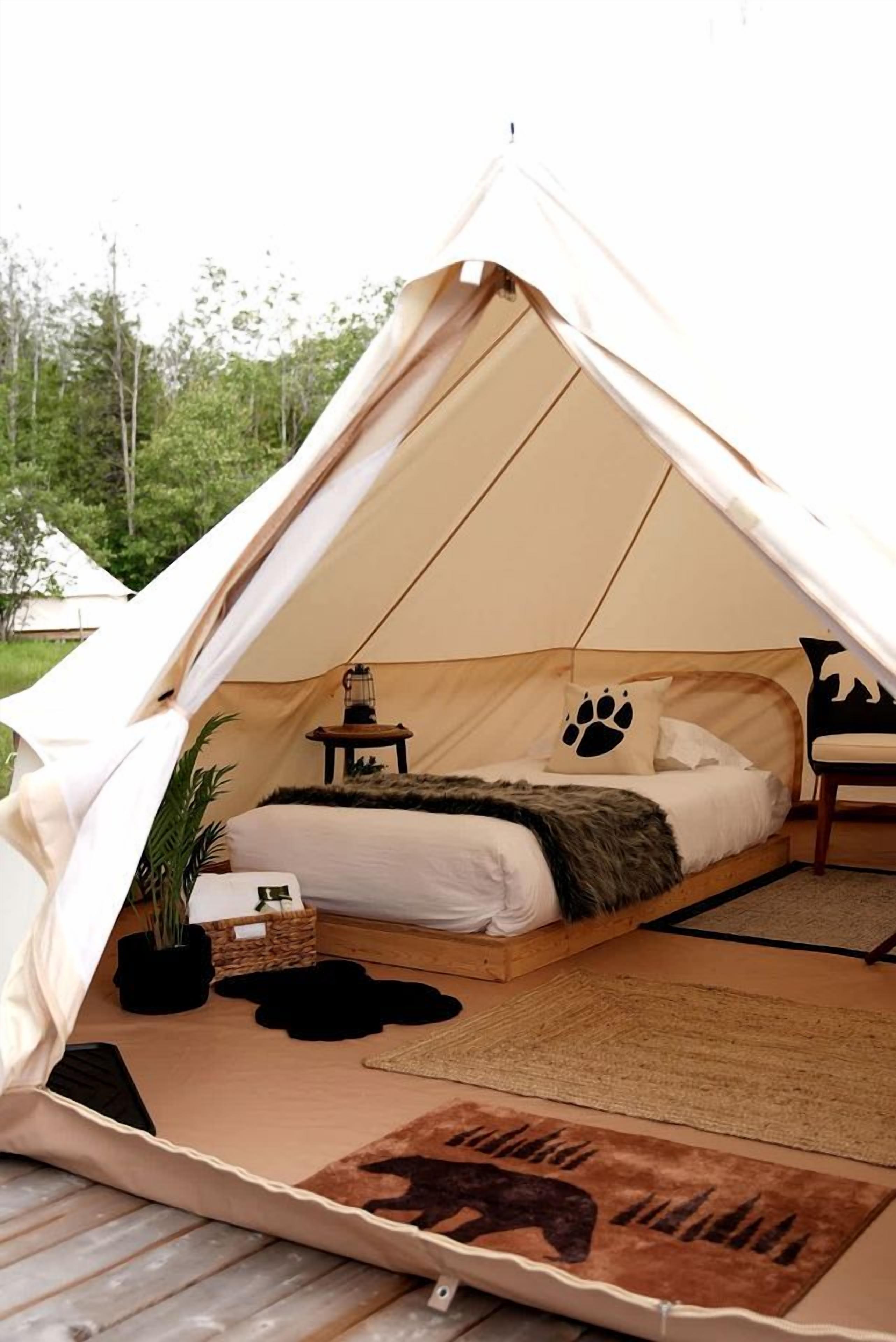 A tent with a bed, a lantern, a chair, and a rug.