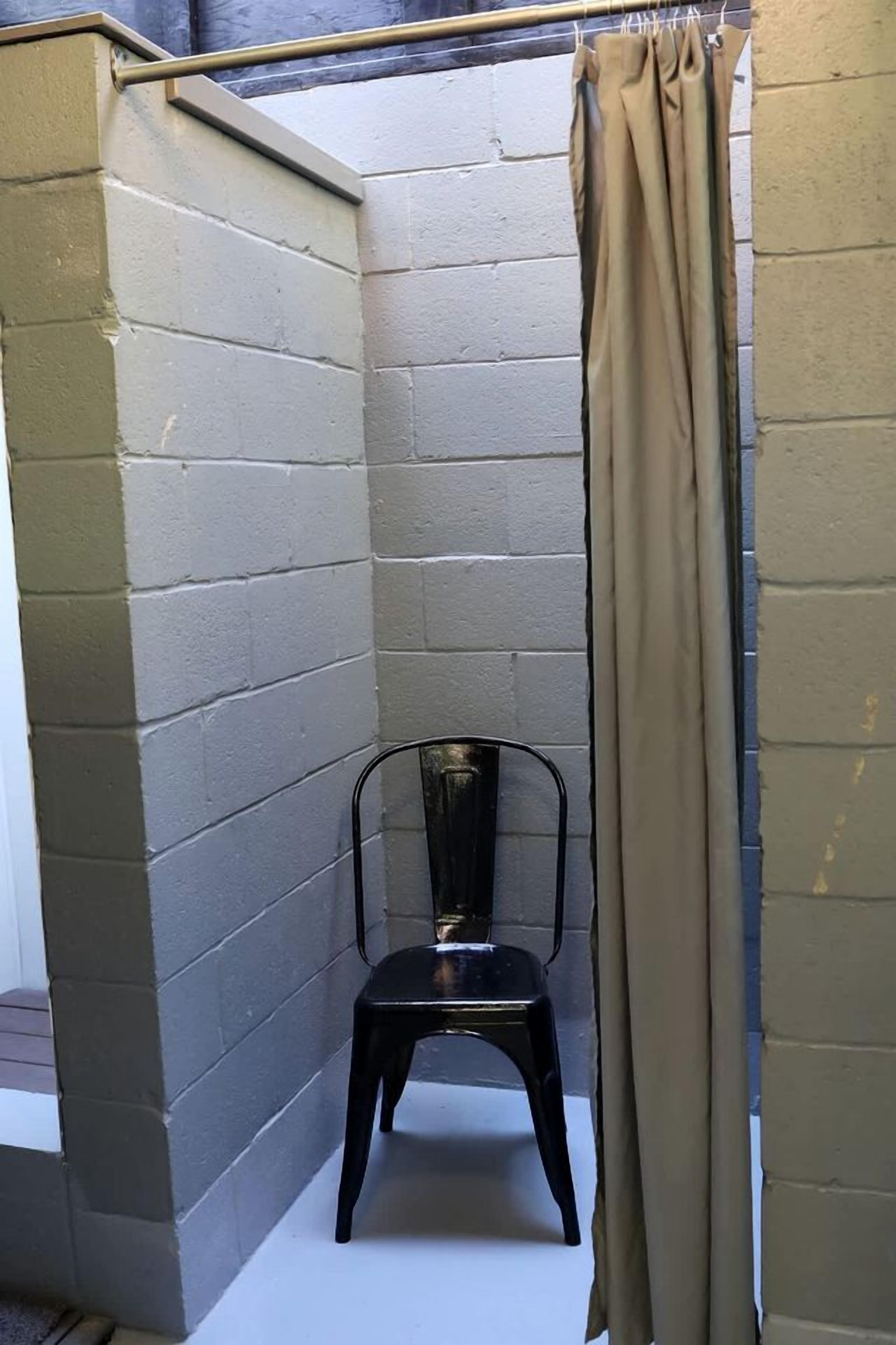A corner room with a black chair, beige curtains, and a metal rod.