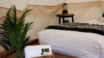 Una carpa con cama, una mesita, una lámpara, una planta en maceta y una cesta.