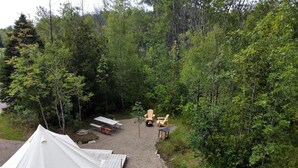 En campingplats med tält, ett bord, stolar och en grusgång, omgiven av träd.