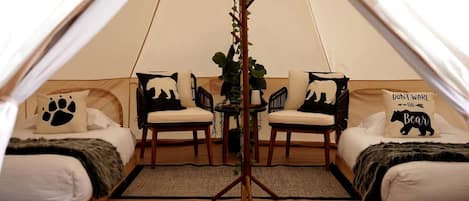 Een gezellige tentkamer met twee bedden, elk voorzien van een beren-thema kussen, een klein tafeltje en een plant.
