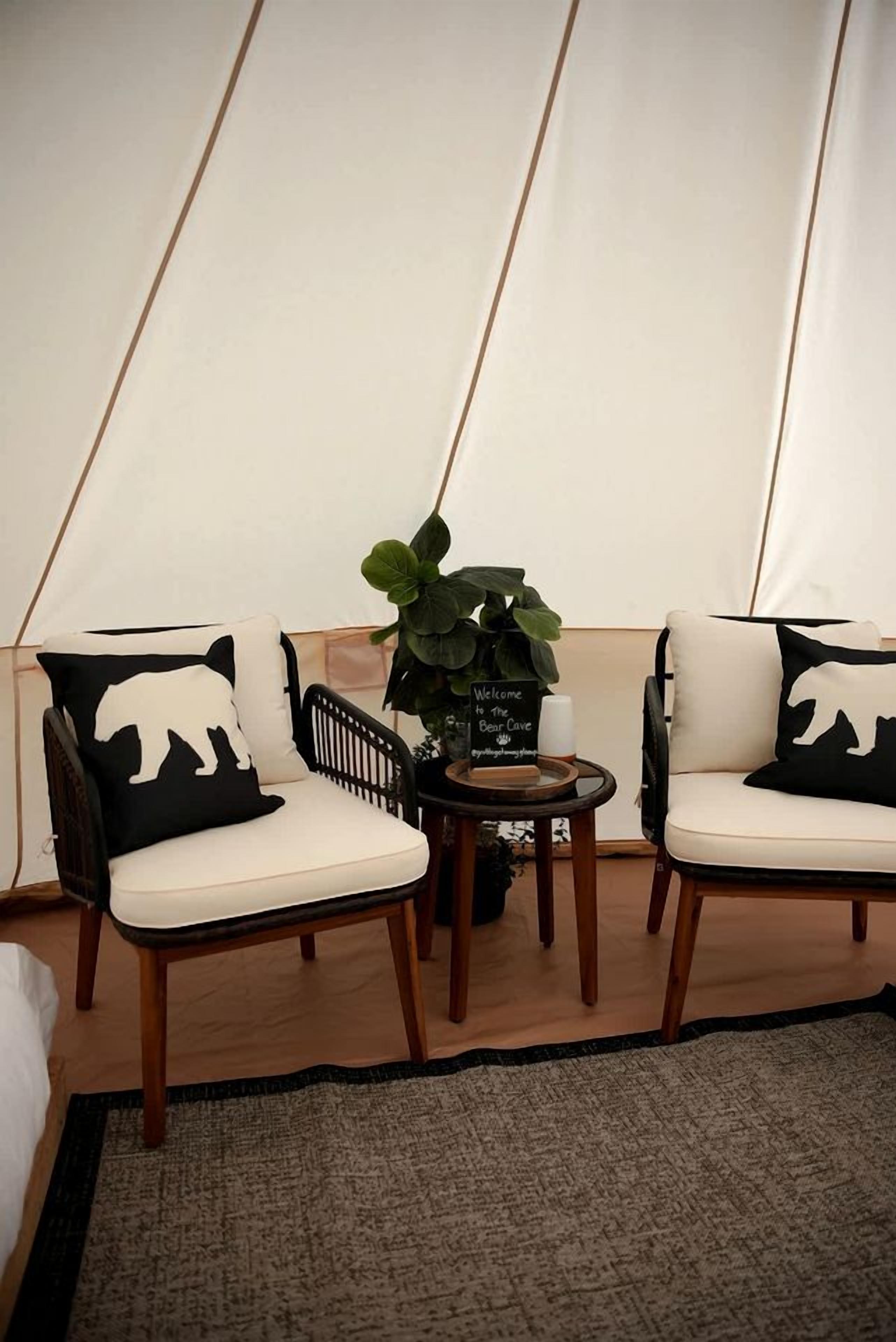 A tented room with two chairs, a small table with a candle, a welcome sign, and a potted plant.