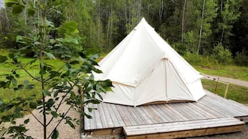 A white tent with a wooden deck in a forested area.
