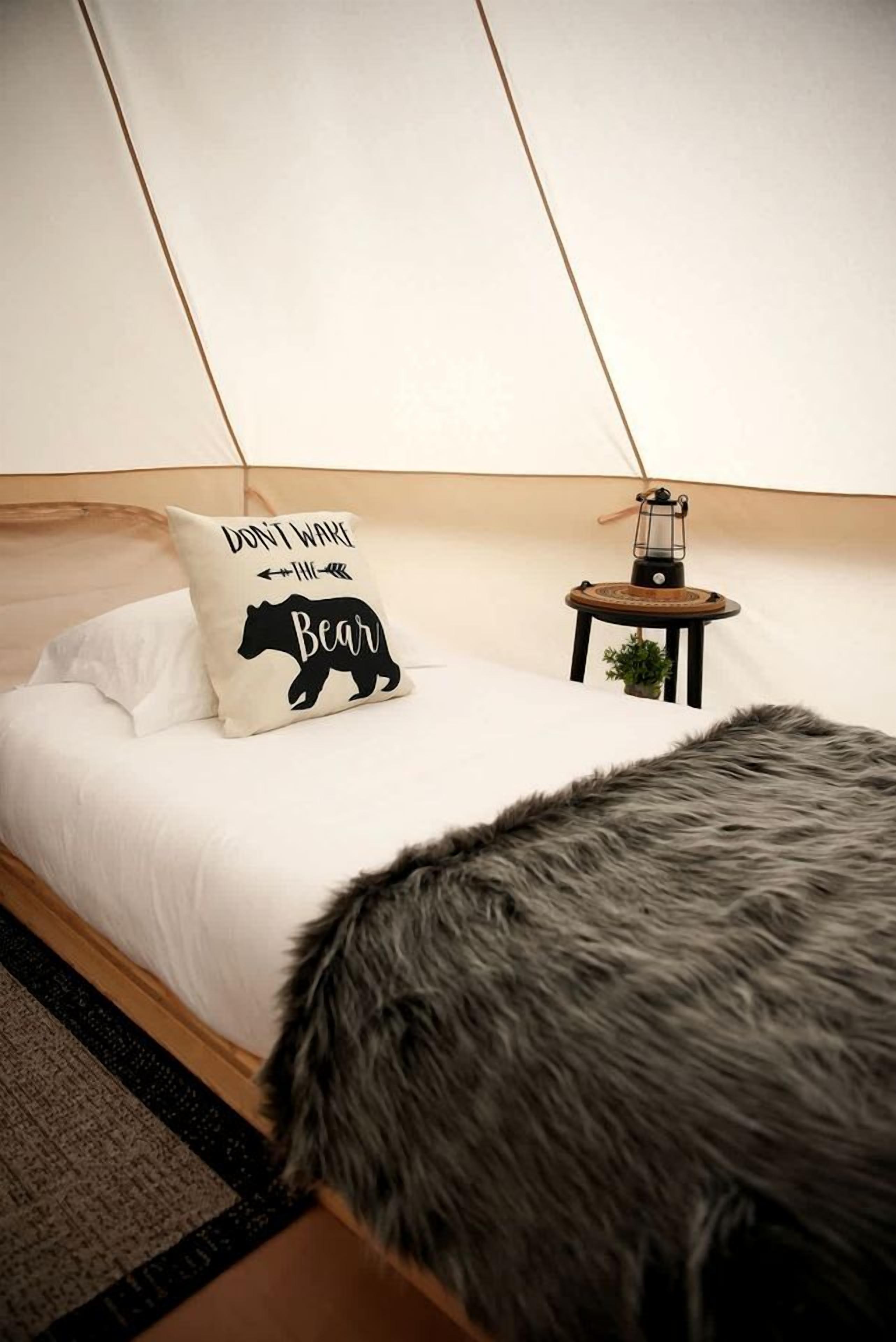 A tented room with a bed, a pillow with bear text, a lantern, and a fur throw.