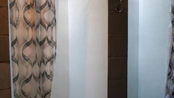 Une salle de bain avec un rideau de douche, un mur blanc et une petite fenêtre.