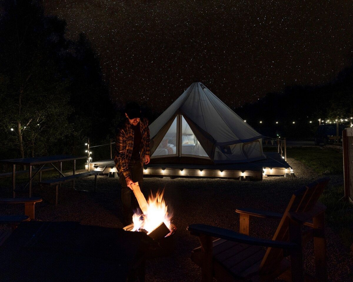 A tent with a fire in front, surrounded by a picnic table and chairs.